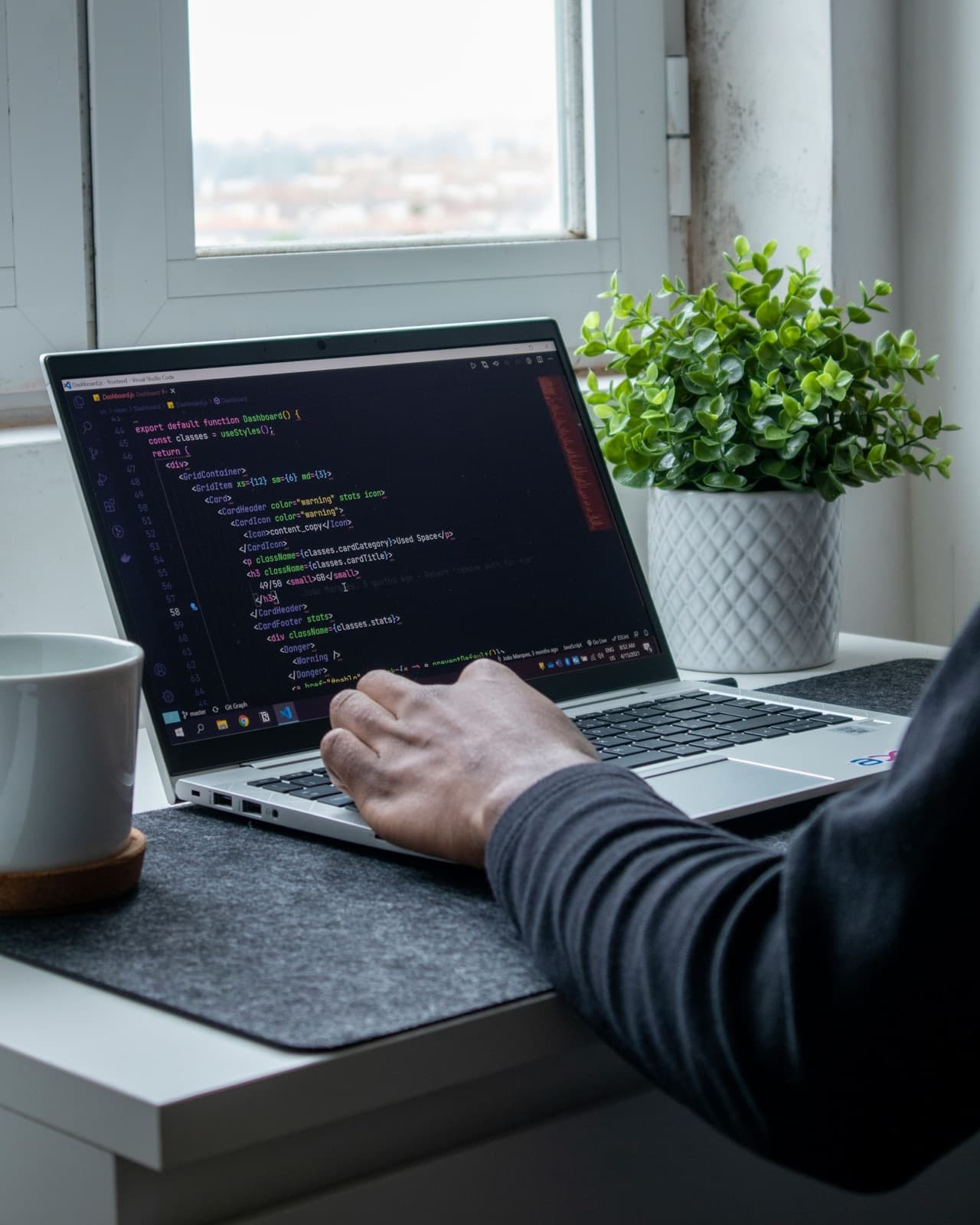 Code on a laptop beside a plant